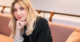 Natalia Albin seated at a table, showcasing a stylish outfit, surrounded by indoor plants in a modern cafe setting.