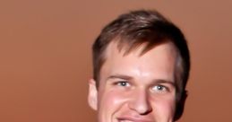 Smiling young man in a navy vest and unique wooden bow tie, capturing a warm sunset backdrop.