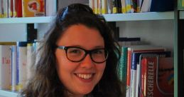 Élise Desbois smiling while holding a book in a cozy library setting, surrounded by shelves of various books.