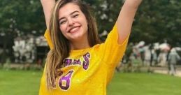 Cheerful woman in a yellow crop top and shorts poses joyfully in a green park, showcasing vibrant summer fashion and confidence.