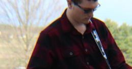 Jalyn Groff performing outdoors with an electric guitar, wearing a black and red plaid shirt and sunglasses.