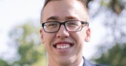 Ethan Ream smiling confidently in a navy suit with a burgundy tie against a lush outdoor background.