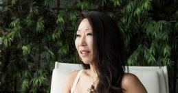 Angie Wang sitting elegantly in a white dress, surrounded by lush greenery, showcasing her stylish and confident demeanor.