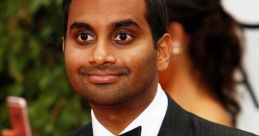 Aziz Ansari smiling in a black tuxedo with a bow tie at a glamorous event surrounded by greenery.