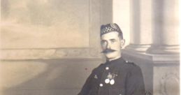 William MacKay, in a formal uniform with medals, seated in a vintage chair, showcasing early 20th-century attire.