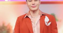 Stylish man in an orange blazer and pink shirt gives a thumbs up, showcasing confidence and modern fashion trends.