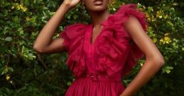 Elegant model poses in a vibrant red ruffled dress surrounded by lush greenery, showcasing bold fashion and style.