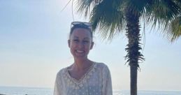 Laura O'Shaughnessy enjoying a sunny beach day in a white dress with palm trees and ocean in the background.