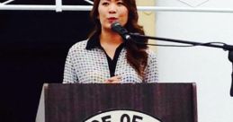 Samar Neweshy delivers a speech at an event, with the Province of Samar seal and floral arrangements in the background.