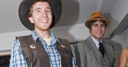 Two men in costumes: one in a cowboy outfit, the other in vintage formal attire, smiling at a lively event.