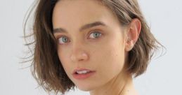 Young woman with short, textured hair and natural makeup, wearing a black sweater with gold embellishments, looking thoughtfully.