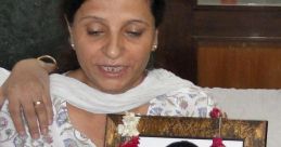 Woman holding a framed portrait of Geetika Sharma, adorned with flower garlands, showcasing remembrance and tribute.