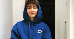 Artel DeVries wearing a blue hoodie, sitting on stairs, exuding a relaxed and casual vibe in a cozy setting.