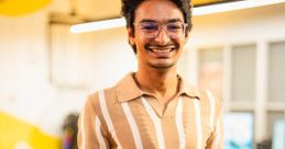 Vatsal Pandya smiling confidently in a stylish striped shirt and gray trousers, set in a modern workspace.