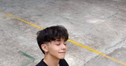 Teen wearing a black shirt and headphones, sitting on a basketball, embodying a carefree attitude with a playful gesture.