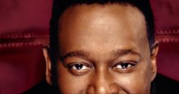 Luther Vandross smiling warmly with hands clasped, showcasing his iconic style and soulful presence in music.