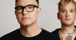 Mark Hoppus and Matt Skiba of blink-182 pose together, showcasing their unique style and band merchandise in a studio setting.