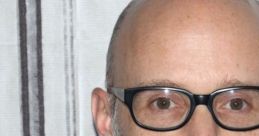 Moby, the American musician and producer, with a gray beard and glasses, poses against a simple background.