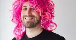 Man with a vibrant pink curly wig, wearing a black t-shirt featuring a stylish "n" logo, exuding a fun and playful vibe.