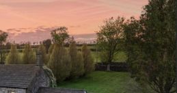 Charming countryside cottage with a lush garden, framed by trees and a stunning sunset sky in the background.