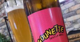 Zigounette au vent bottle with pink label beside a glass of blonde beer on a rustic table. Enjoy this refreshing brew!