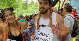 Two friends celebrate with "Calma, Calabreso" signs, playful costumes, and a lively crowd in a festive outdoor setting.