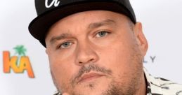 Charlie Sloth poses confidently, wearing a black cap with "Ghost" and a stylish patterned shirt, showcasing his signature style.