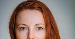 Portrait of a woman with long red hair and green eyes, wearing a dark green top, embodying elegance and confidence.