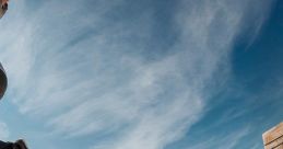 Skateboarder performing an impressive jump over a wooden ramp under a blue sky with wispy clouds.