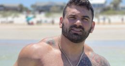 Muscular man with tattoos at the beach, wearing colorful swim trunks, showcasing confidence and summer vibes.