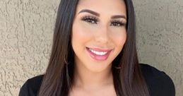 Smiling Latina woman in a stylish black outfit, showcasing long hair and vibrant makeup, exuding confidence and charm.