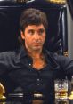 Tony Montana, iconic character from Scarface, sits confidently in a lavish chair with a drink, embodying 1980s crime drama style.