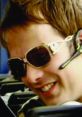 Nathan Barley smiling in stylish sunglasses, showcasing his quirky and confident personality from the cult TV series.