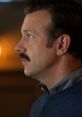 Ted Lasso in a thoughtful moment, showcasing his signature mustache and sweater in Season 1's heartfelt scenes.