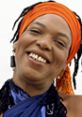 Miss Cleo smiling with vibrant orange headwrap and colorful attire, embodying her captivating psychic persona.