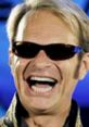 David Lee Roth smiling widely in sunglasses, showcasing his energetic personality and rock star charisma.