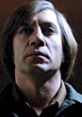 Close-up of Anton Chigurh from No Country for Old Men, capturing his intense and menacing expression in low lighting.