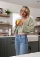 Kallmekris, wearing a cozy green cardigan and jeans, enjoys a yellow mug in a modern kitchen setting.