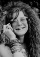 Janis Joplin smiling, adorned with bracelets and stylish sunglasses, capturing her iconic 1960s rock and roll spirit.