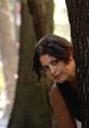 Woman peeking from behind a tree, evoking intrigue and mystery, reflective of themes in "Wild Canaries Trailer.