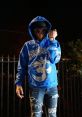 Young individual wearing a blue Sugarhillddot hoodie and distressed jeans, striking a confident pose at night.