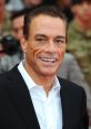 Jean-Claude Van Damme smiles at a red carpet event, showcasing his charismatic persona and stylish black suit.