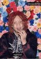 Trippie Redd in a floral backdrop, wearing a graphic hoodie and silver chains, showcasing his unique style.