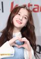 Nancy from Momoland making a heart gesture, showcasing her charming personality and vibrant energy at a promotional event.