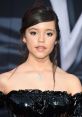 Jenna Ortega at a red carpet event, showcasing her elegant style with a shiny black off-shoulder dress and delicate jewelry.