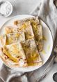 Delicious lemon-scented poppy seed crepes drizzled with olive oil, served on a white plate with a rustic napkin.