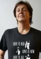 Paul McCartney wearing a black t-shirt with "Love is old, love is new" text, showcasing his iconic style and music legacy.