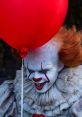 Pennywise the Clown from *It* (2017) grinning menacingly under a bright red balloon, embodying chilling horror.