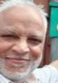 Smiling older man with gray beard and light shirt, showcasing warmth and friendliness in a casual outdoor setting.