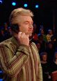 Host on the set of Deal Or No Deal UK, engaged in a phone call while contestants and audience watch intently.